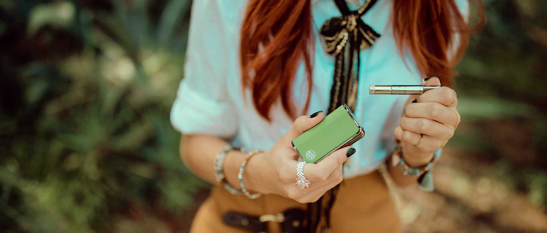 Red haired girl with white shirt holding a green Wulf Duo Wax pen outside at a park